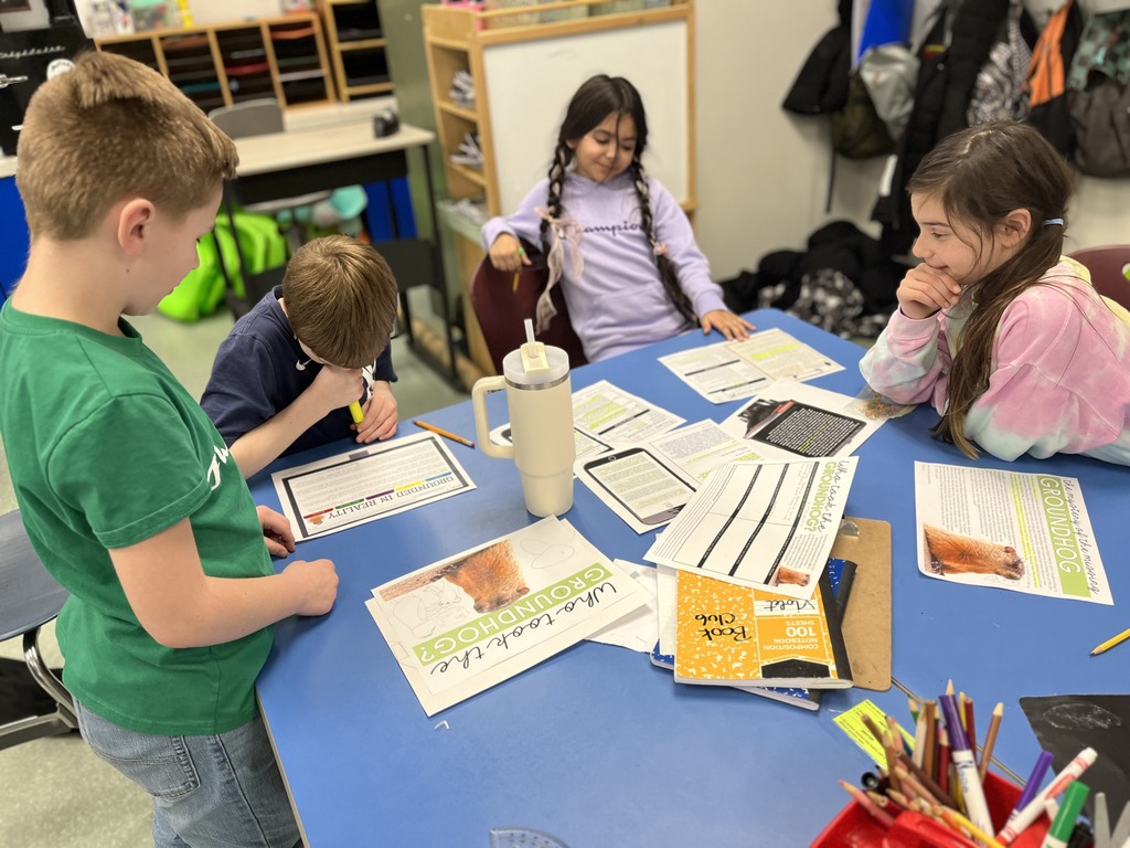 Image of students sitting at a blue table with documents in front of them