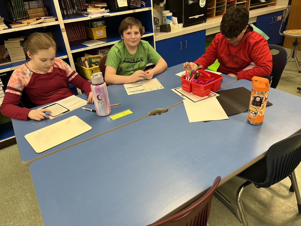 Image of students sitting at a blue table with documents in front of them