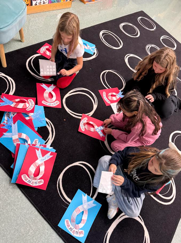 Students sit on a black carpet to assemble decorations for a Veterans Day event