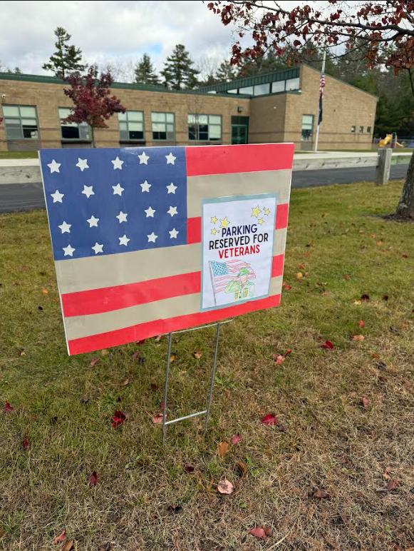 Image of an American Flag  sign post that has a student decorated sign that reads "Parking reserved for veterans"