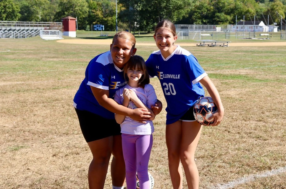Three girls pose for a photo on a field