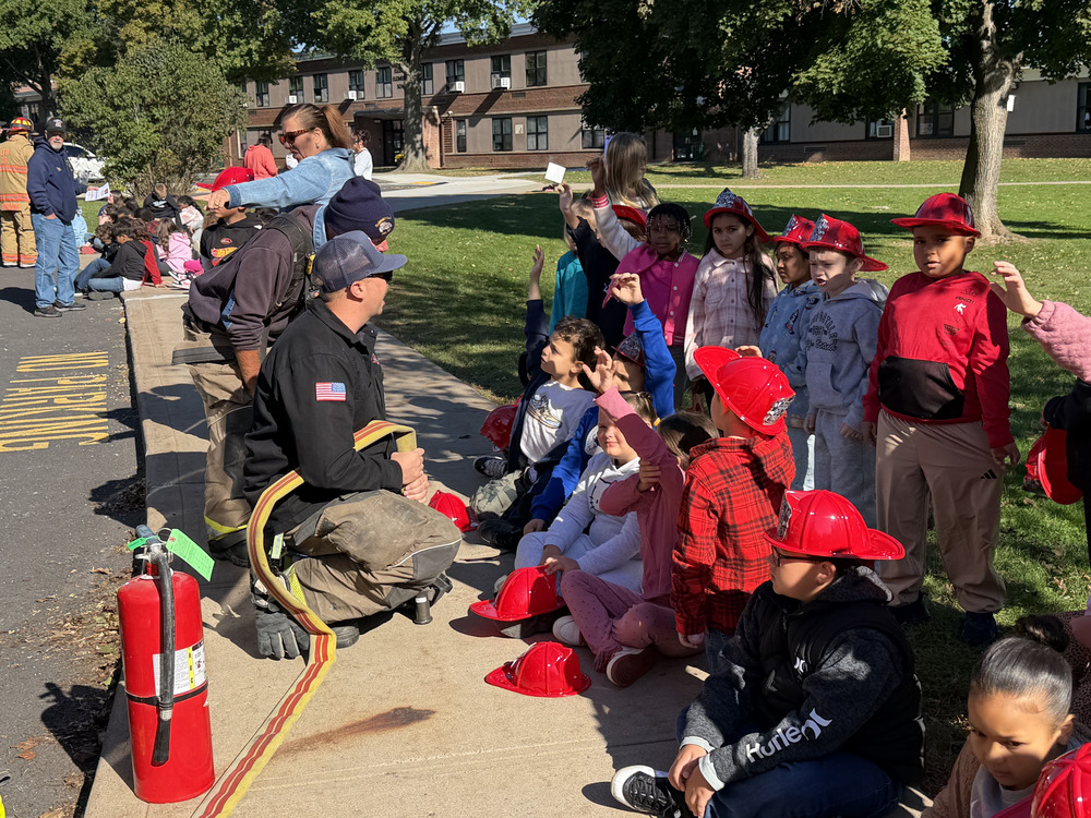 A firefighter kneels down in front of a group of students on a sidewalk