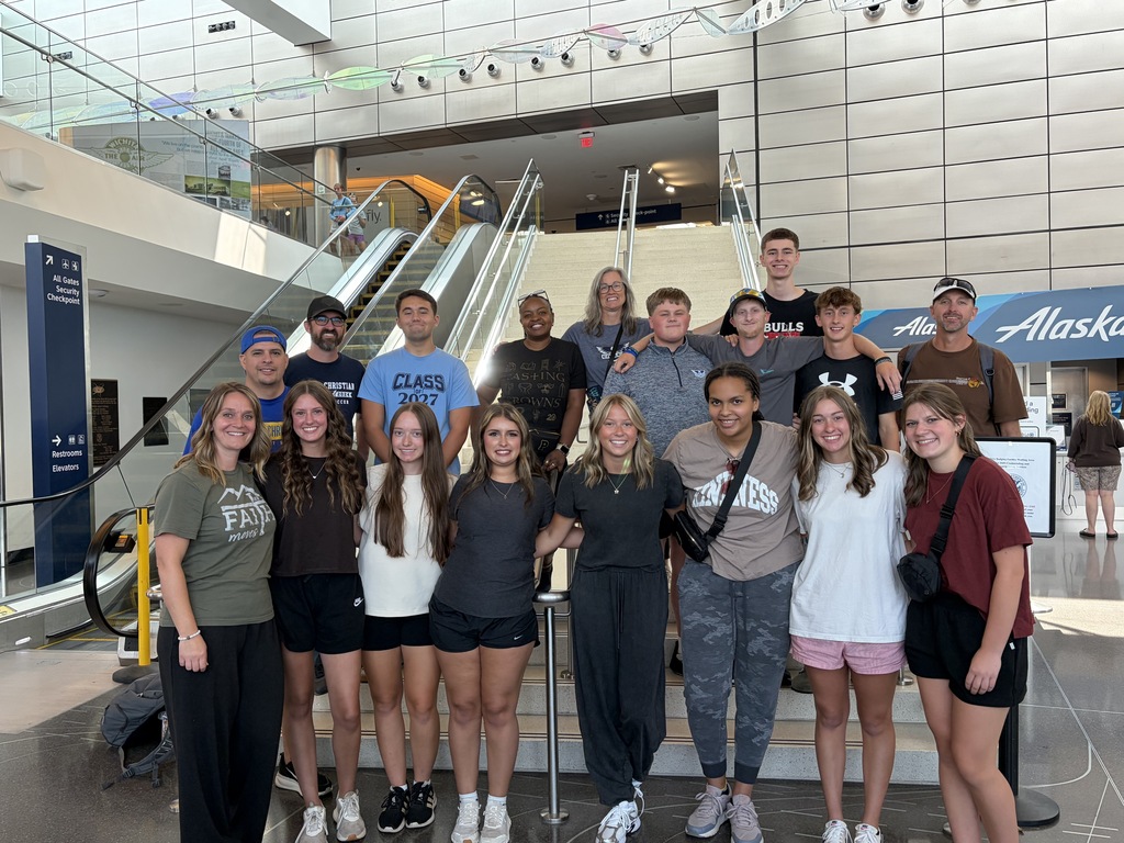A group of people, including adults and children, pose for a photo in an indoor space with escalators.