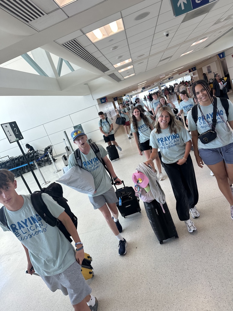 A group of individuals, wearing matching shirts, walk in an airport with luggage and bags.