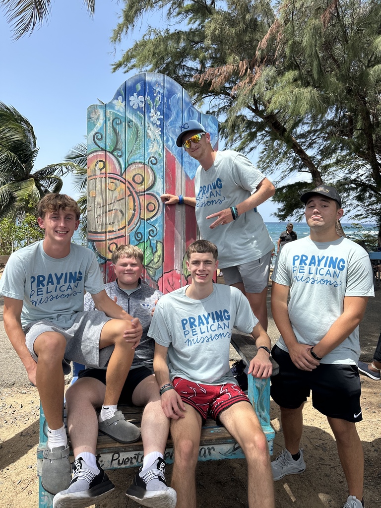 Five people wearing matching shirts and shorts pose in front of a colorful beach chair.