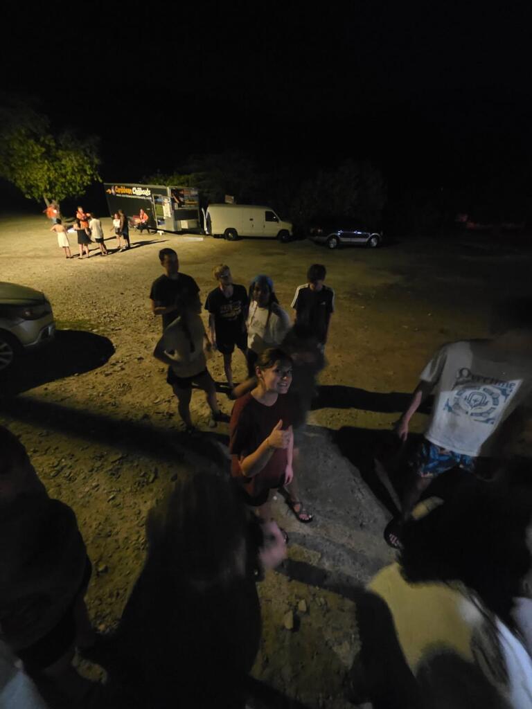 Group of people gathered outside at night, some standing near a food truck and others in a circle.