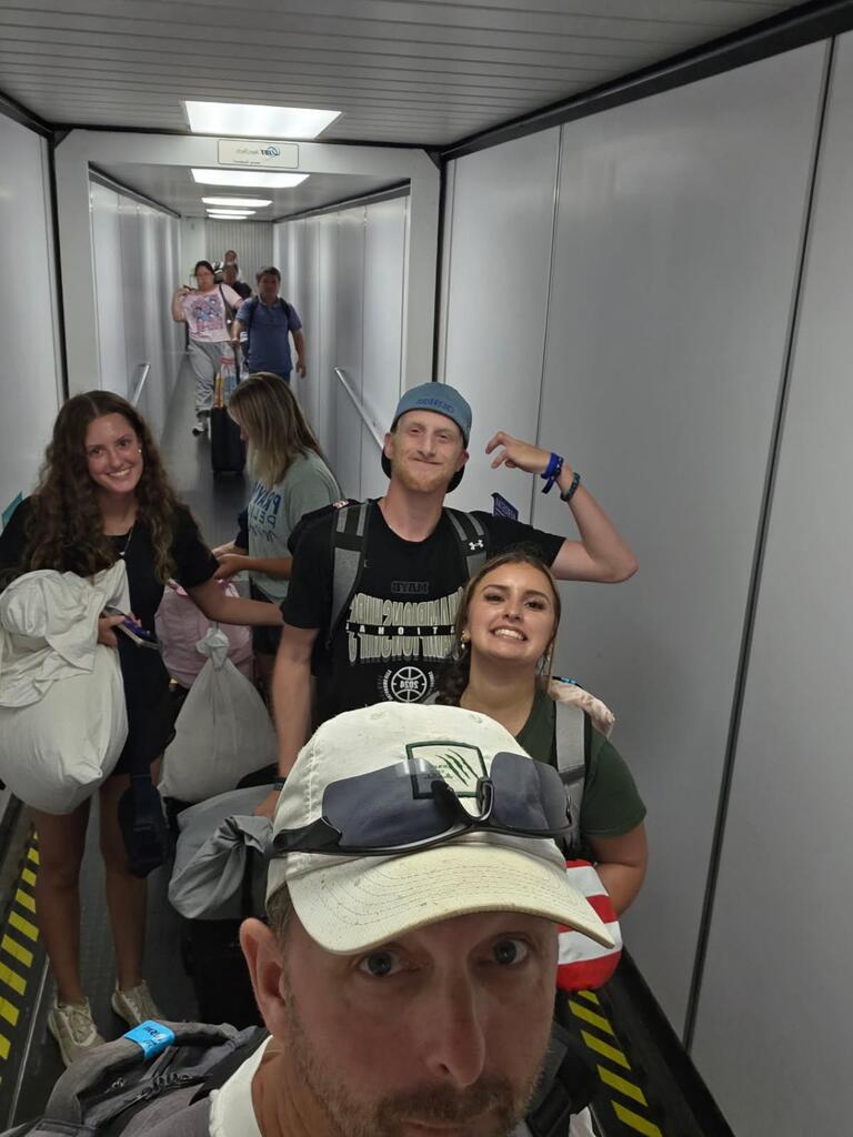 A group of people with luggage in a narrow hallway, one person taking a selfie with others in the background.