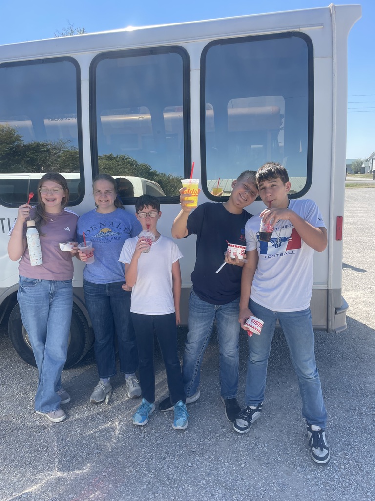 Five kids, some holding ice cream, pose in front of a white bus under a clear sky.