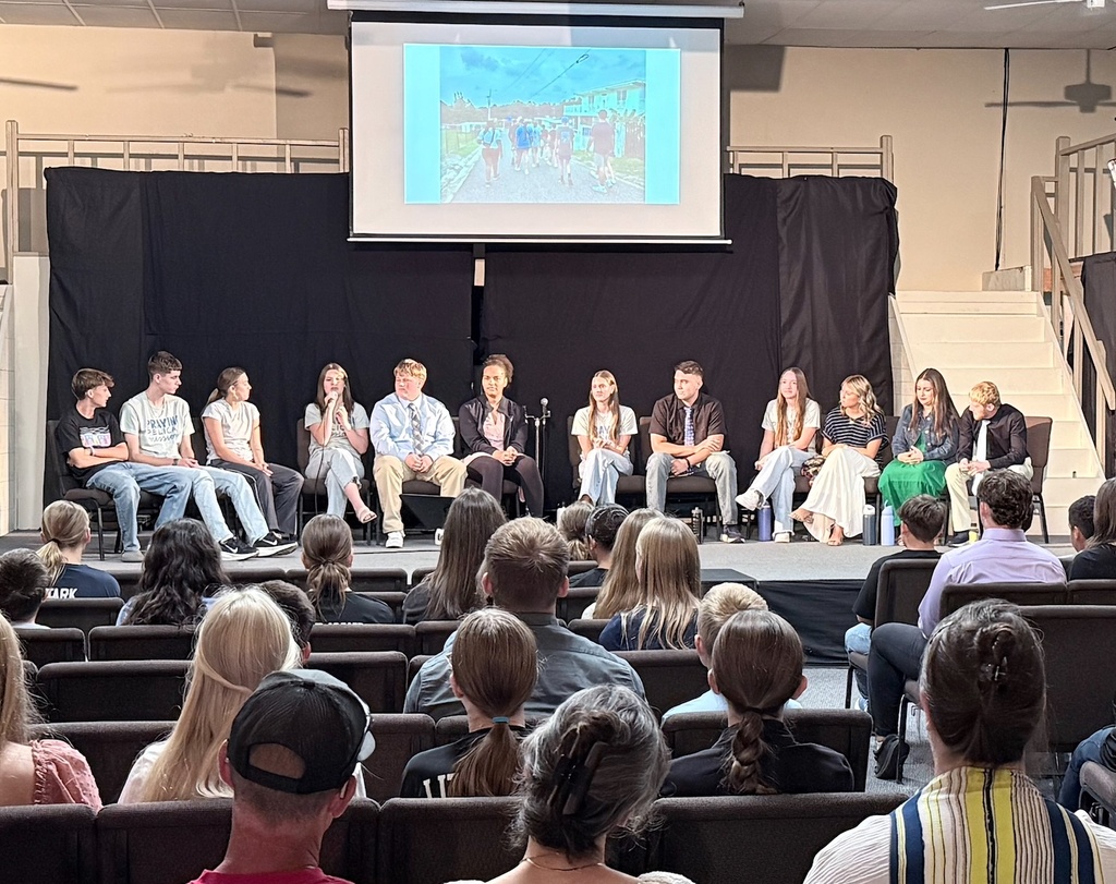 A group of people sitting in rows on chairs, watching a presentation on a stage.