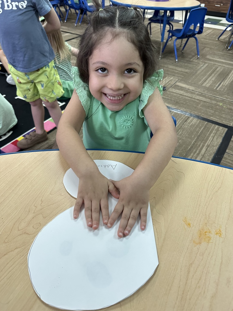 Little girl in a green shirt, smiling big & holding her butterfly art