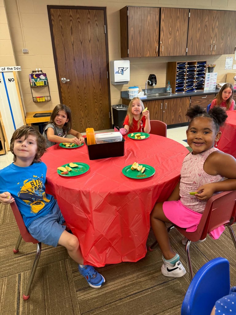 Children sitting at tables enjoying apple slices