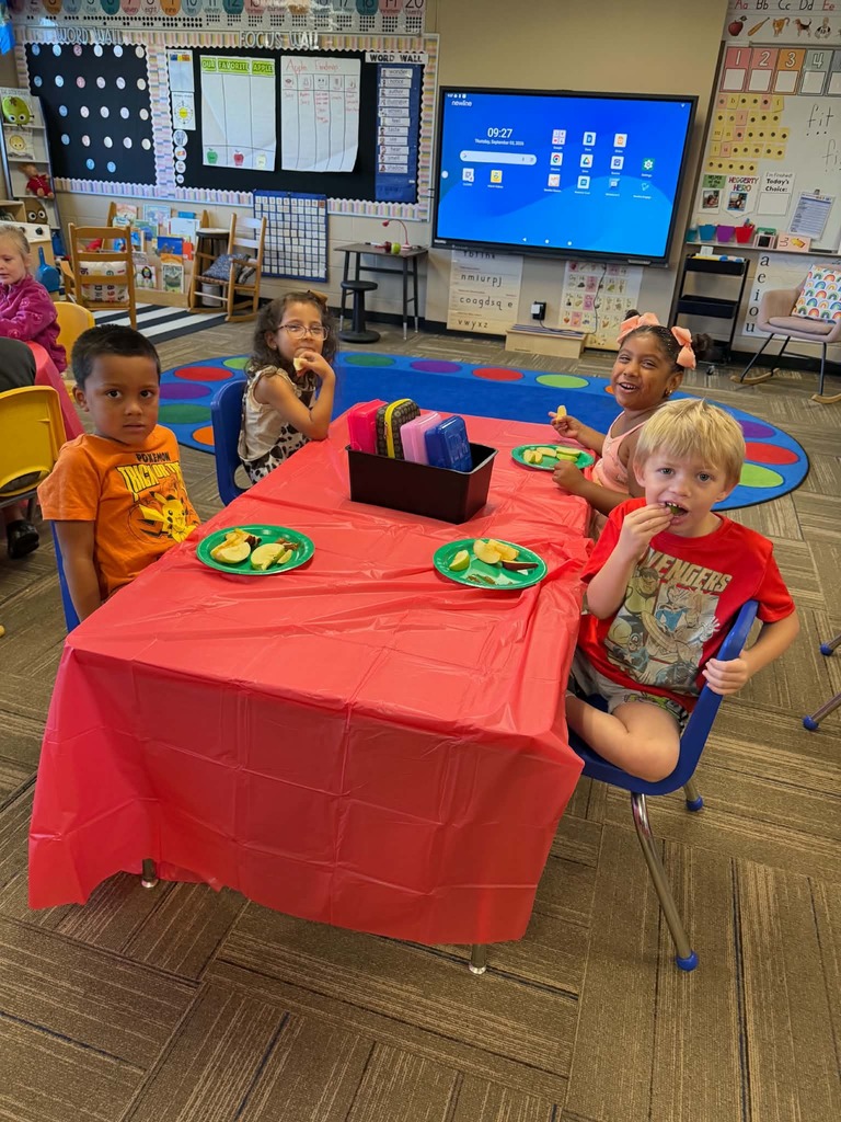 Children sitting at tables enjoying apple slices
