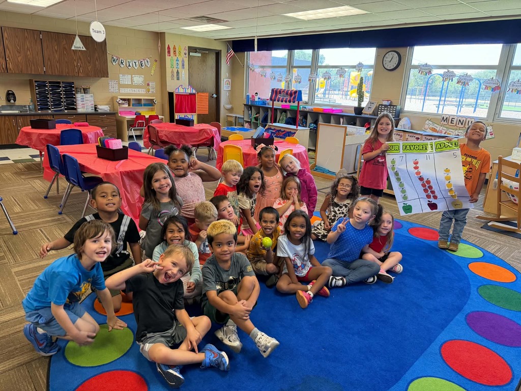 Kindergarten sitting on the rug showing their graph results for their favorite apples
