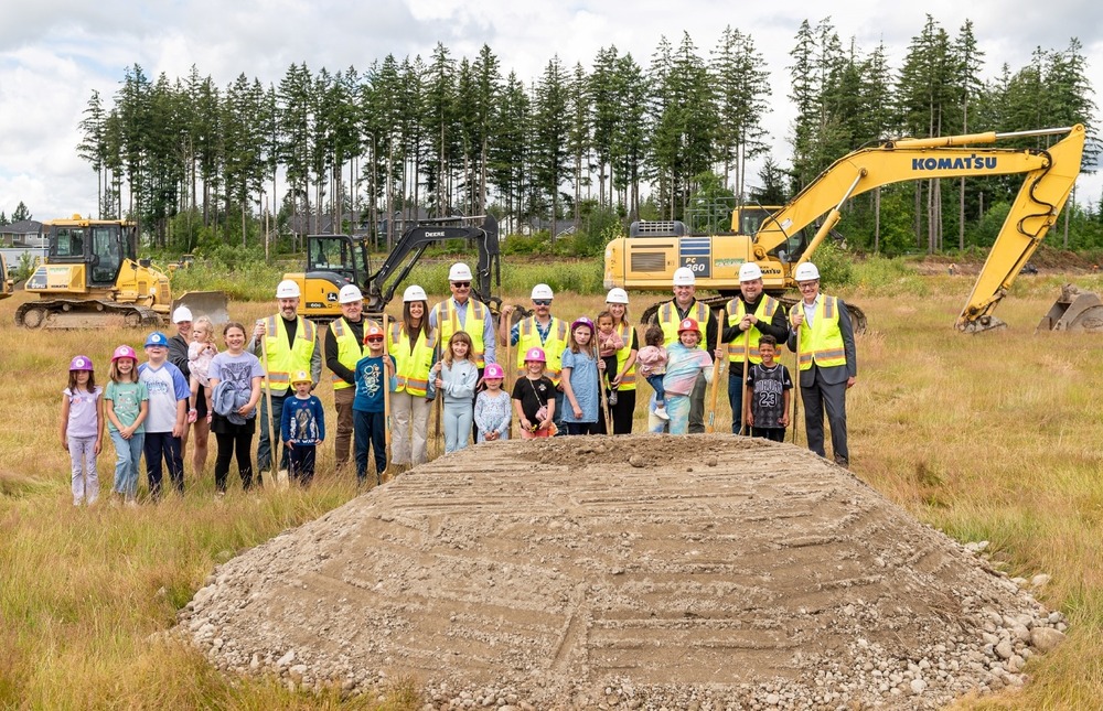students, school board, superi;ntendents and city officials stand with shovels at the ground breaking ceremony for Evergreen Elementary with contruction equipment and the school site in the background