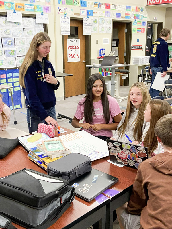high school student looking over the shoulder of middle school students in a group seated at a desk working together on a Chromebook