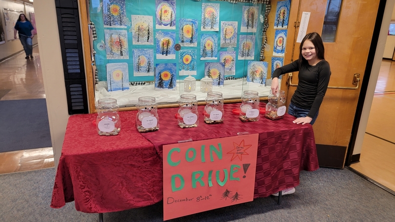 Image of student at a table filled with coin jars and a sign that reads coin drive!