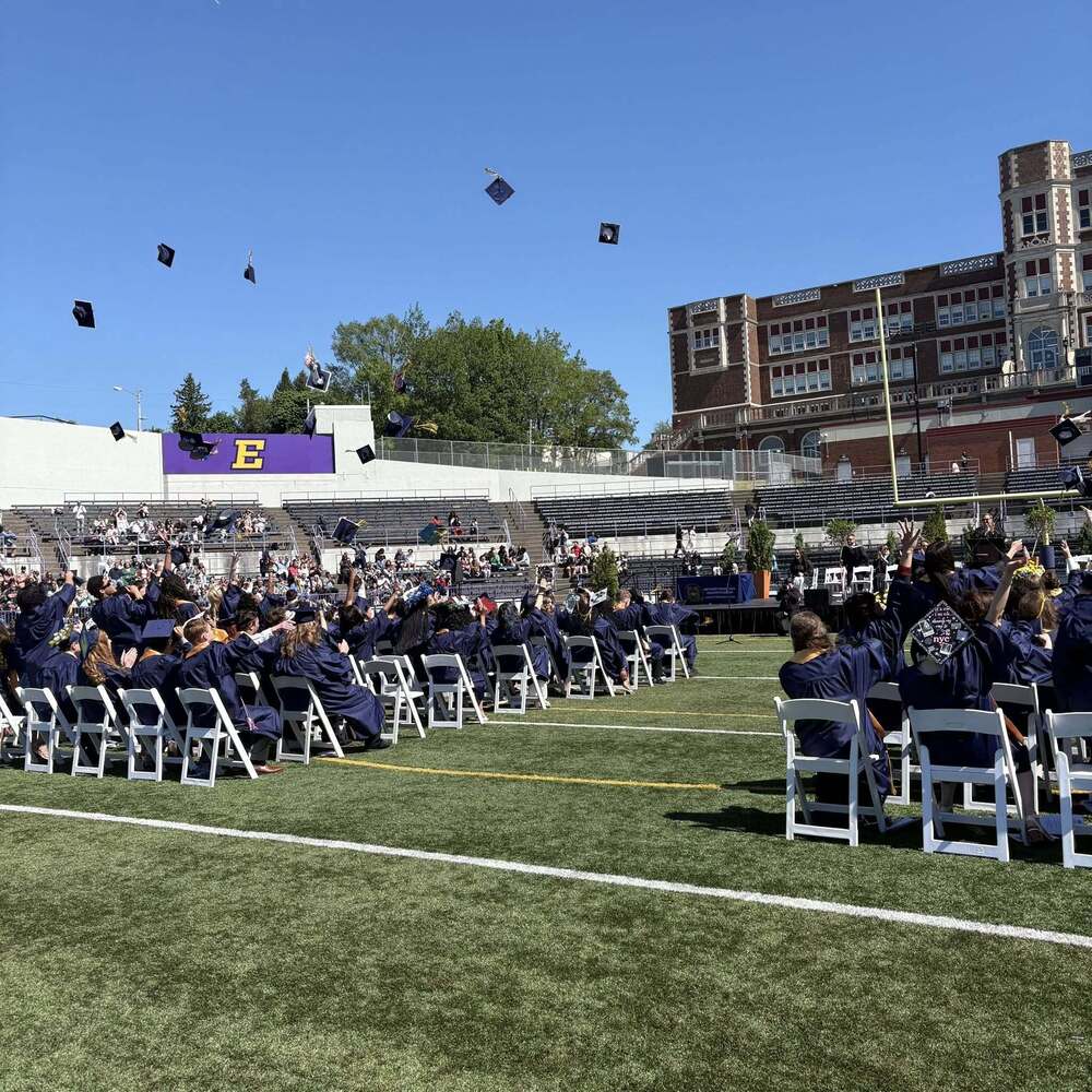 Erie's Public Schools graduates throwing their caps as they graduate on the field.