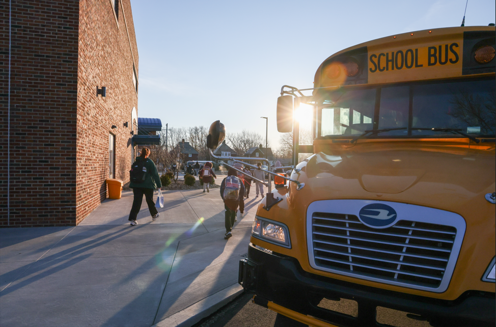 Students walking to school with a school bus in the far right corner. 