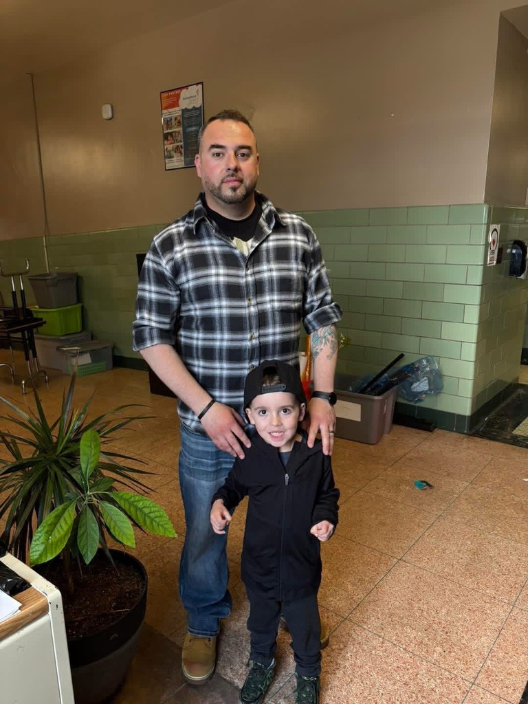 A man and child are staying by each other in the school building In  the front of the inside door.