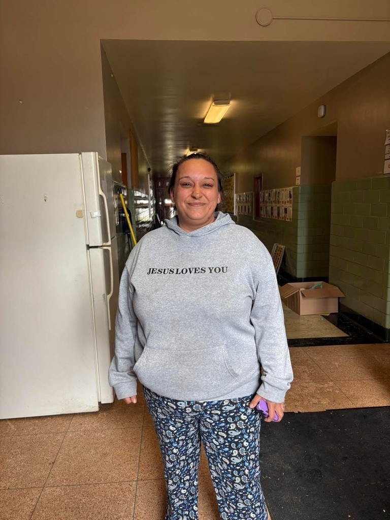 A woman is standing and wearing a grey sweater 
