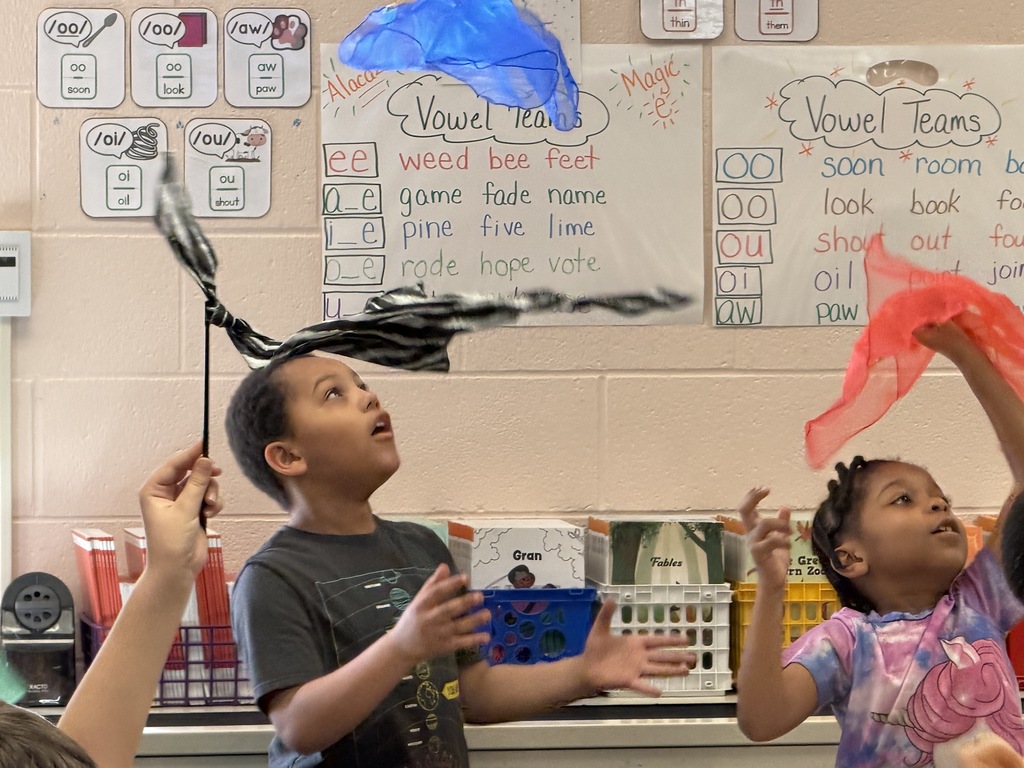 A student looking up at a blue mesh cloth falling back down so he can catch it. 