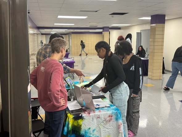 Students looking at items on a table in a hall. 