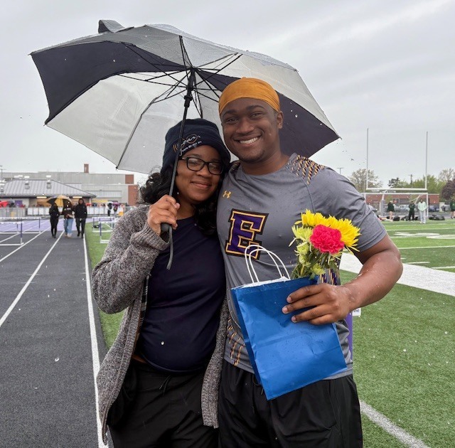 Mother and son standing outside while they hold a umbrella. 