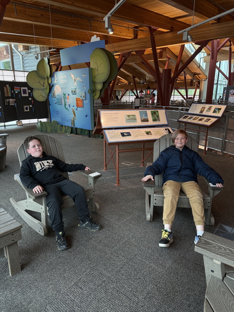 Two students sitting in Adirondack chairs with informational signs in the background 