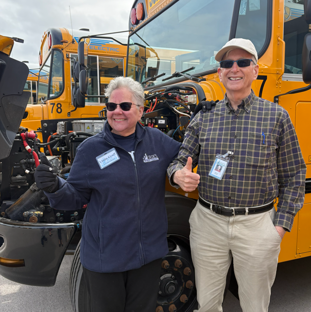 Director Linda Graff and Director Sumner Nicholas holding a thumbs up in front of a school bus that has its hood open.