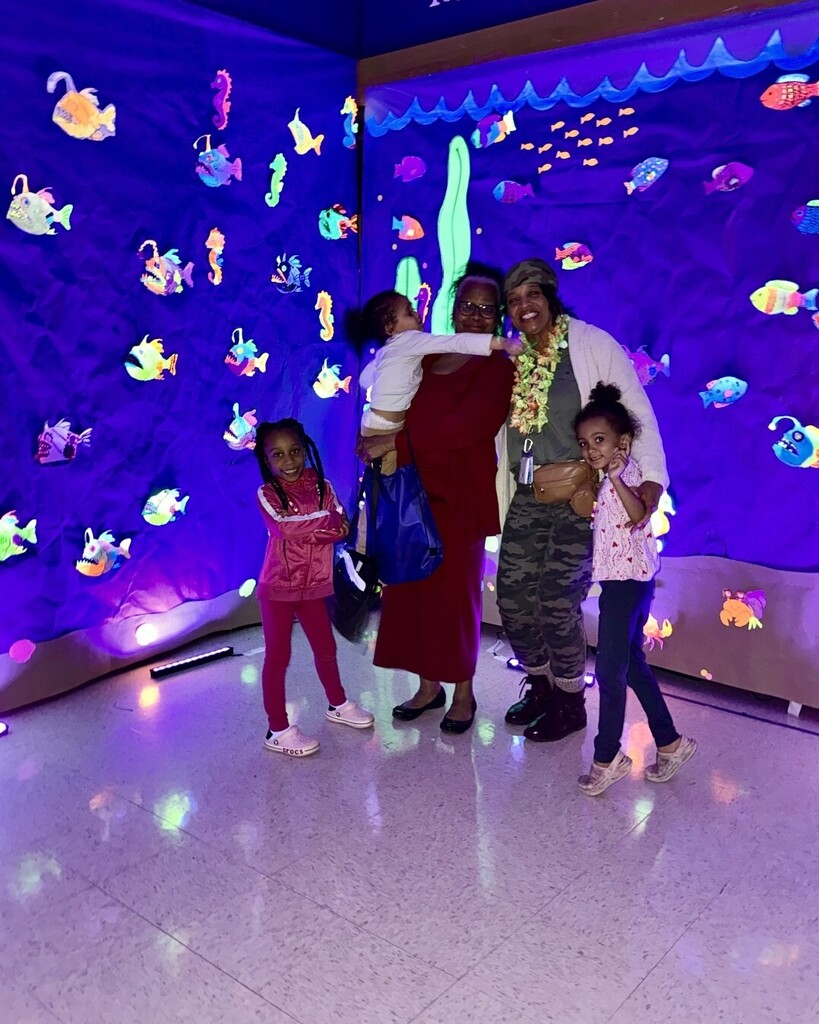family in front of black light art display glowing fish/reef