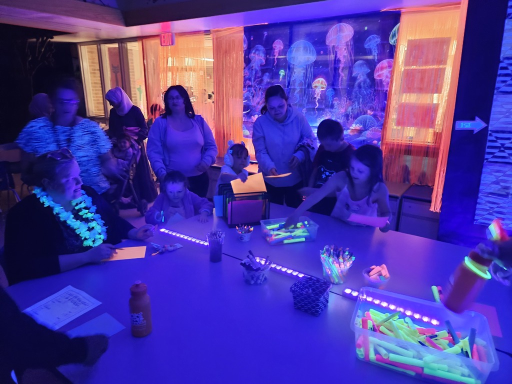 families creating art in black light area of art show in library