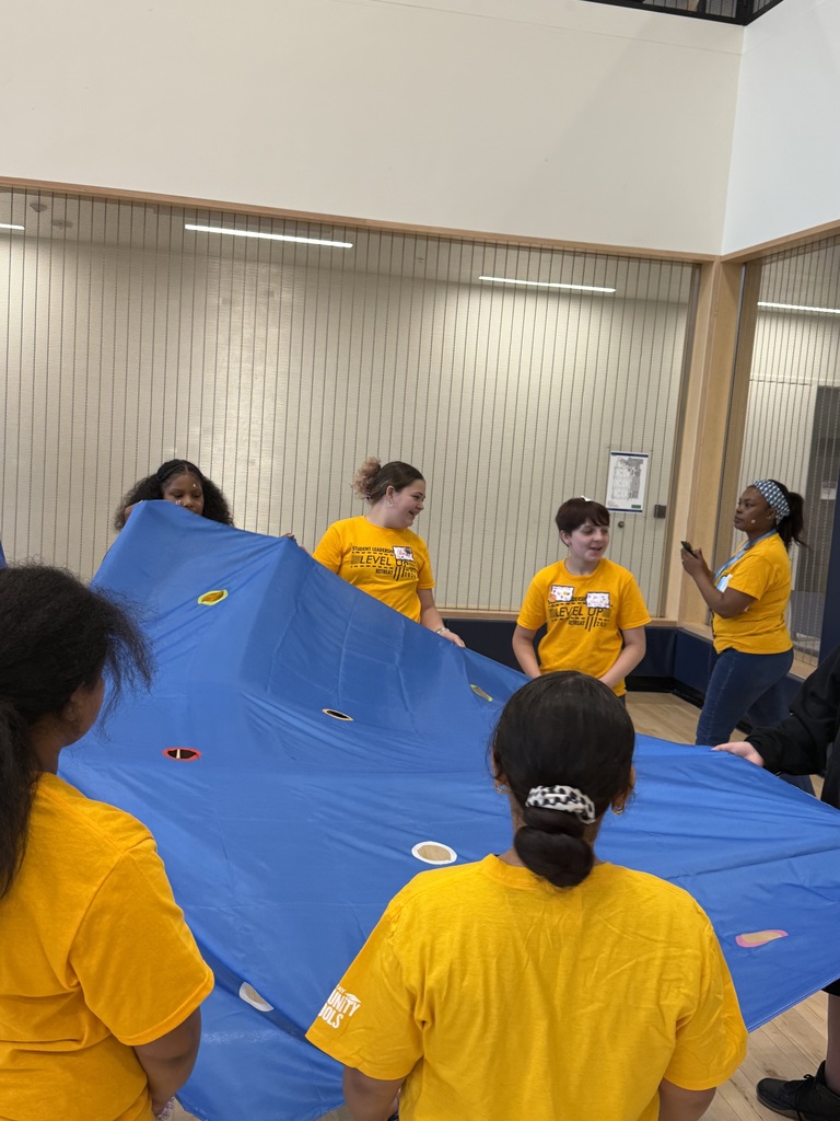 Edison students play a game using a parachute with holes in it and working as a team to roll balls into the matching colored holes.