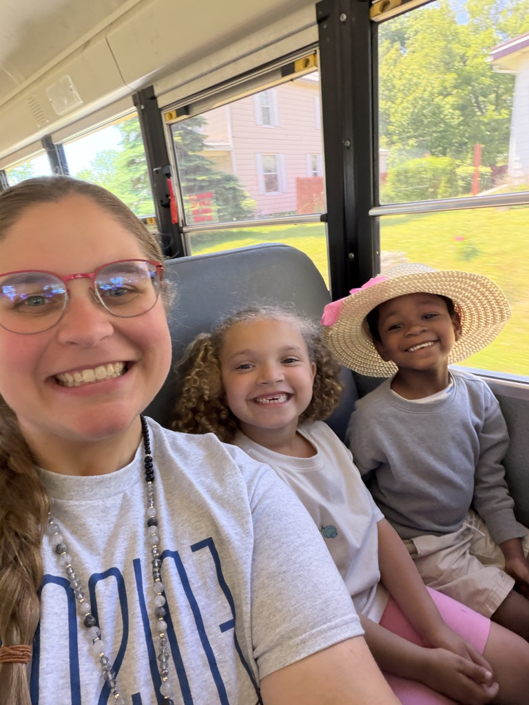 Two smiling students sitting with their teacher on the bus.