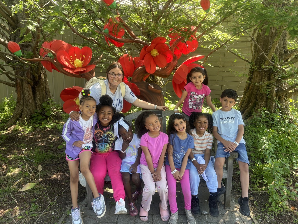 Students posing with their teacher in front of giant flowers at the zoo.