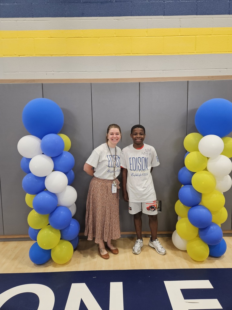 Student standing with teacher in between two columns of blue, yellow, and white balloons.
