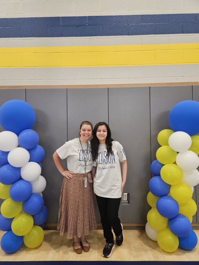Student standing with teacher in between two columns of blue, yellow, and white balloons.