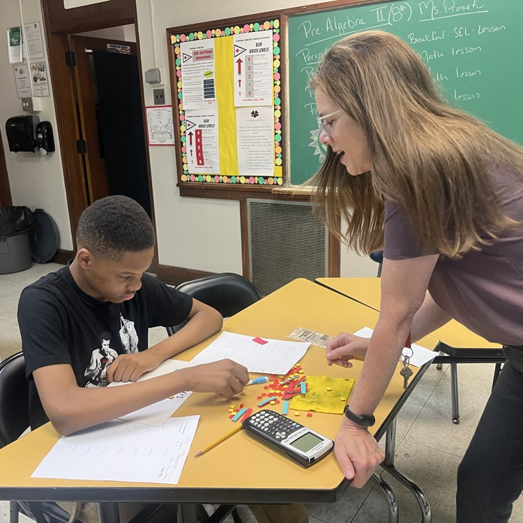 A women helping a student who is doing math with tiles.