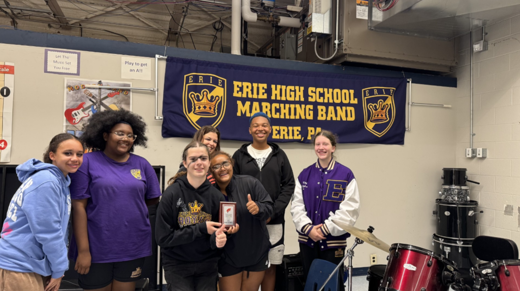 Erie High Marching Band students posing for a photo while two students hold a plaque. 