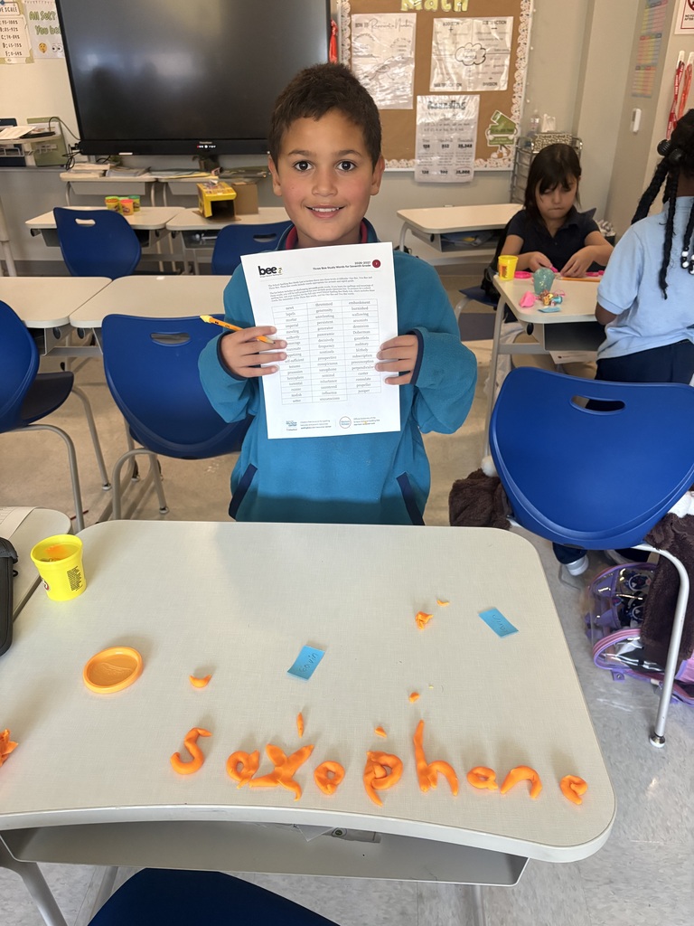Student holding up a list of his spelling words. On the desk in front of him is the word "saxophone".