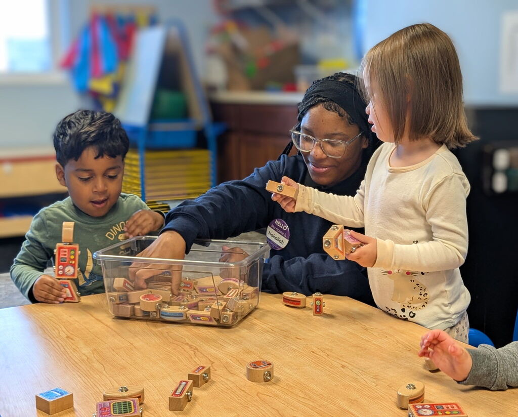 Erie High student playing with blocks with two children in the toddler room.