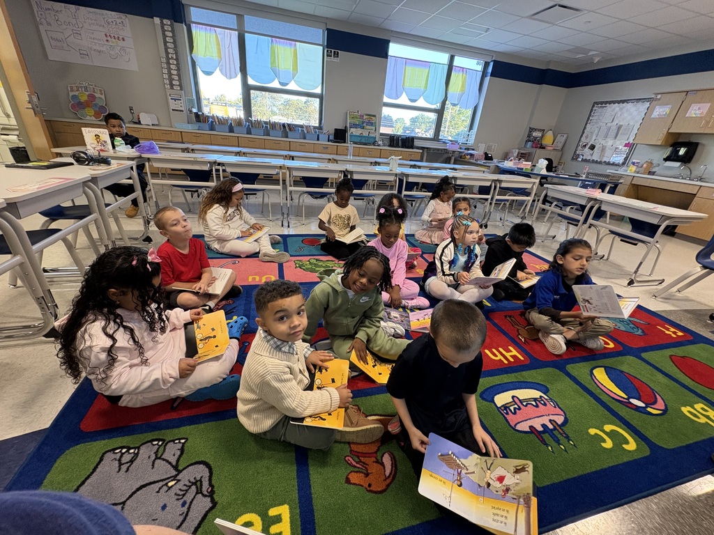 Students sitting on the carpet holding books.