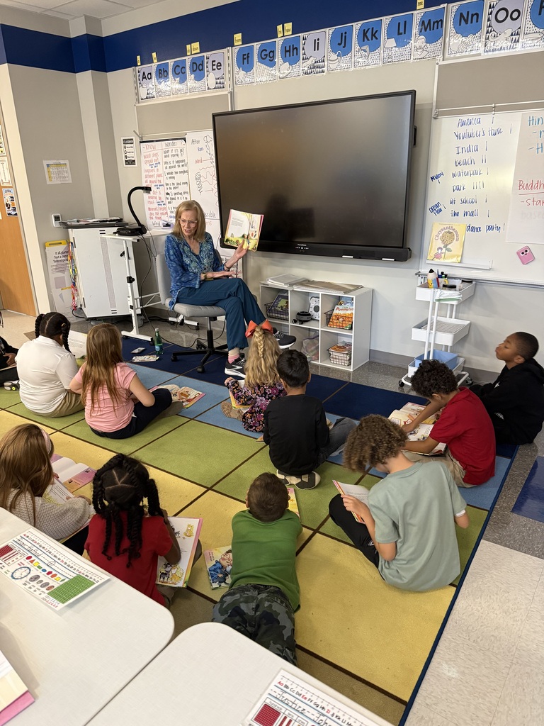 Guest reader holding up the book she is reading to show the children sitting on the floor the pictures.