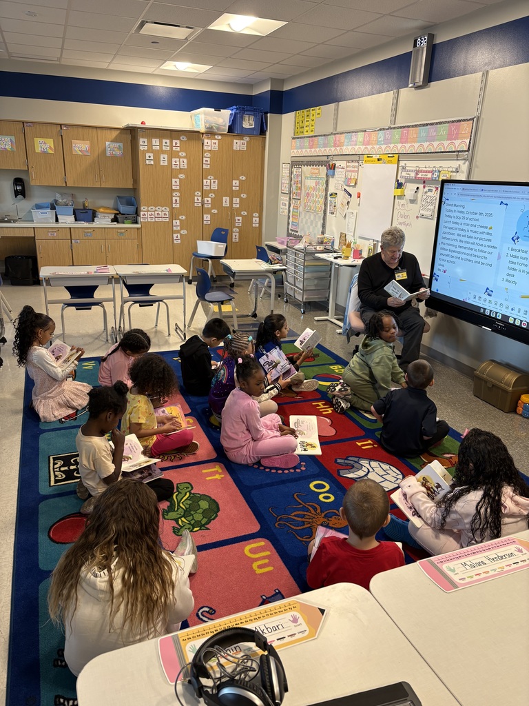 Students sitting on the floor listening to a guest reader.