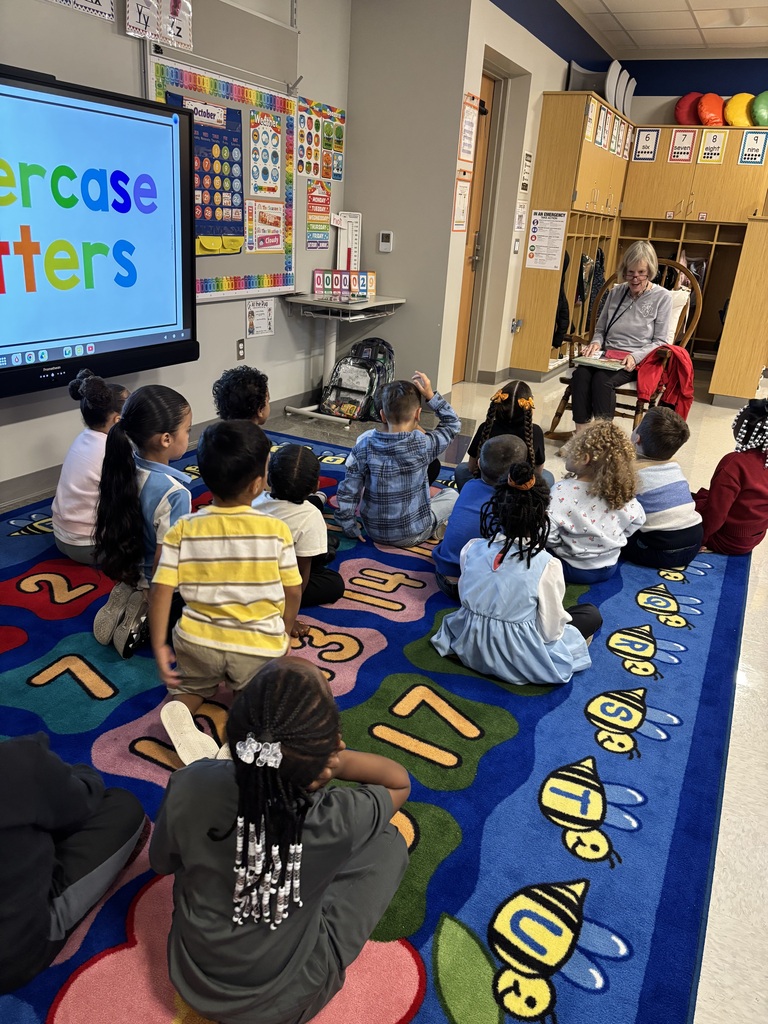 Students sitting on the floor listening to a guest reader.