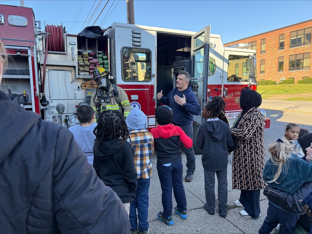 Students listening to a firefighter speak, in front of the firetruck