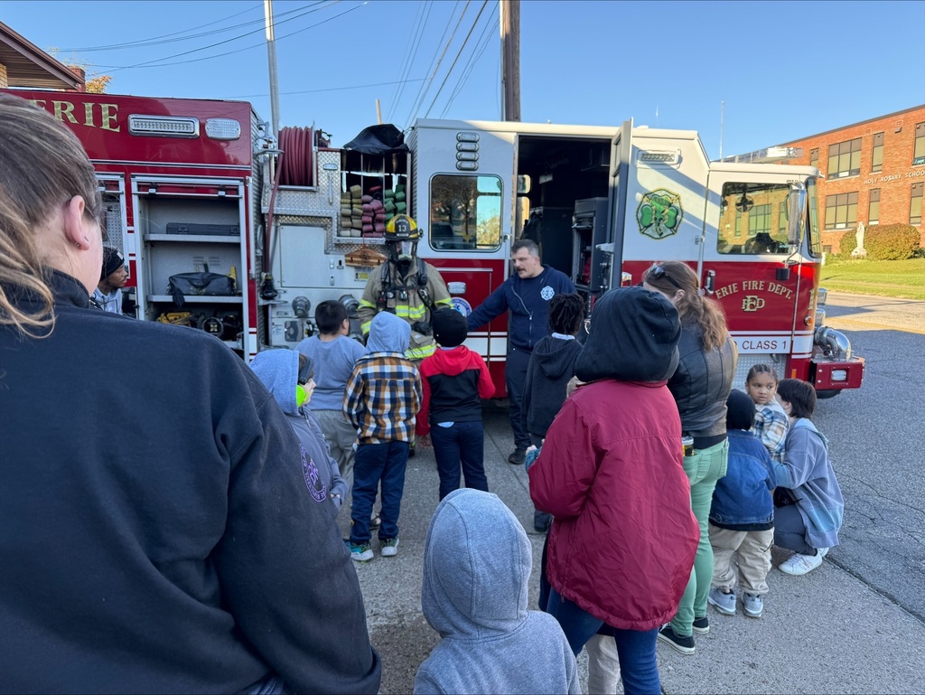 Students listening to a firefighter speak, in front of the firetruck
