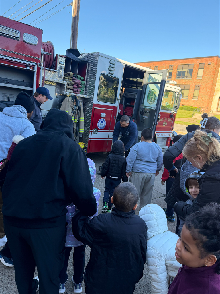 Students listening to a firefighter speak, in front of the firetruck