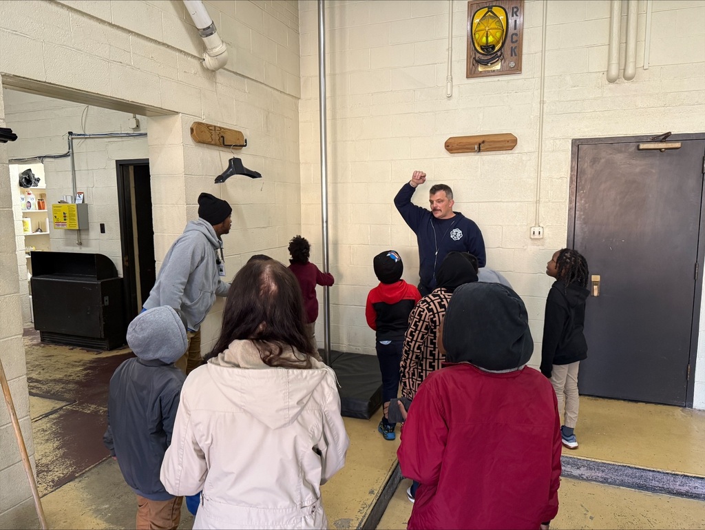 Students listening to a firefighter speak, in the firehouse