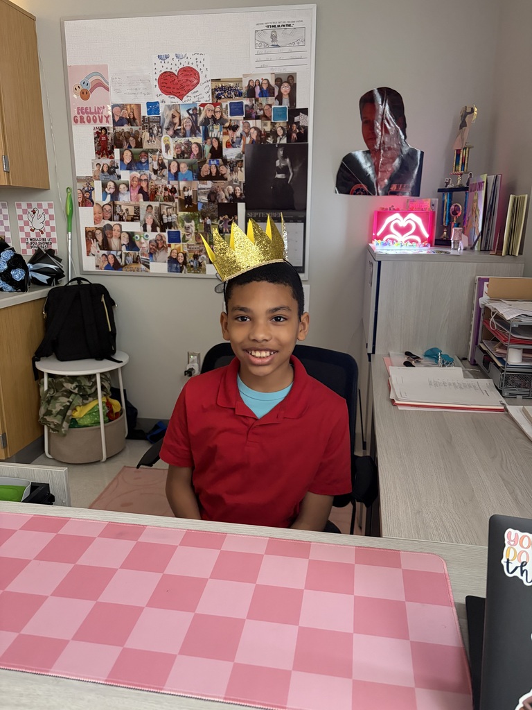 Male student sitting at the teacher's desk, wearing a crown