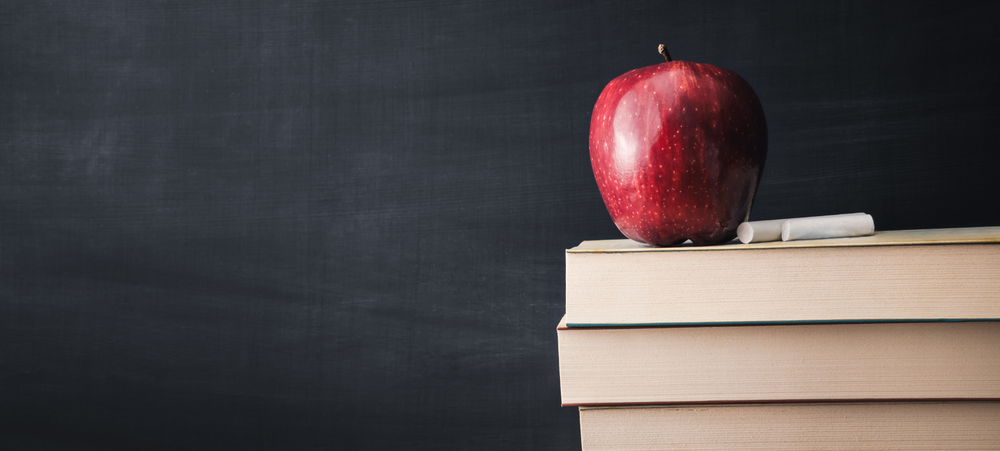 Chalkboard with books, chalk, and an apple.